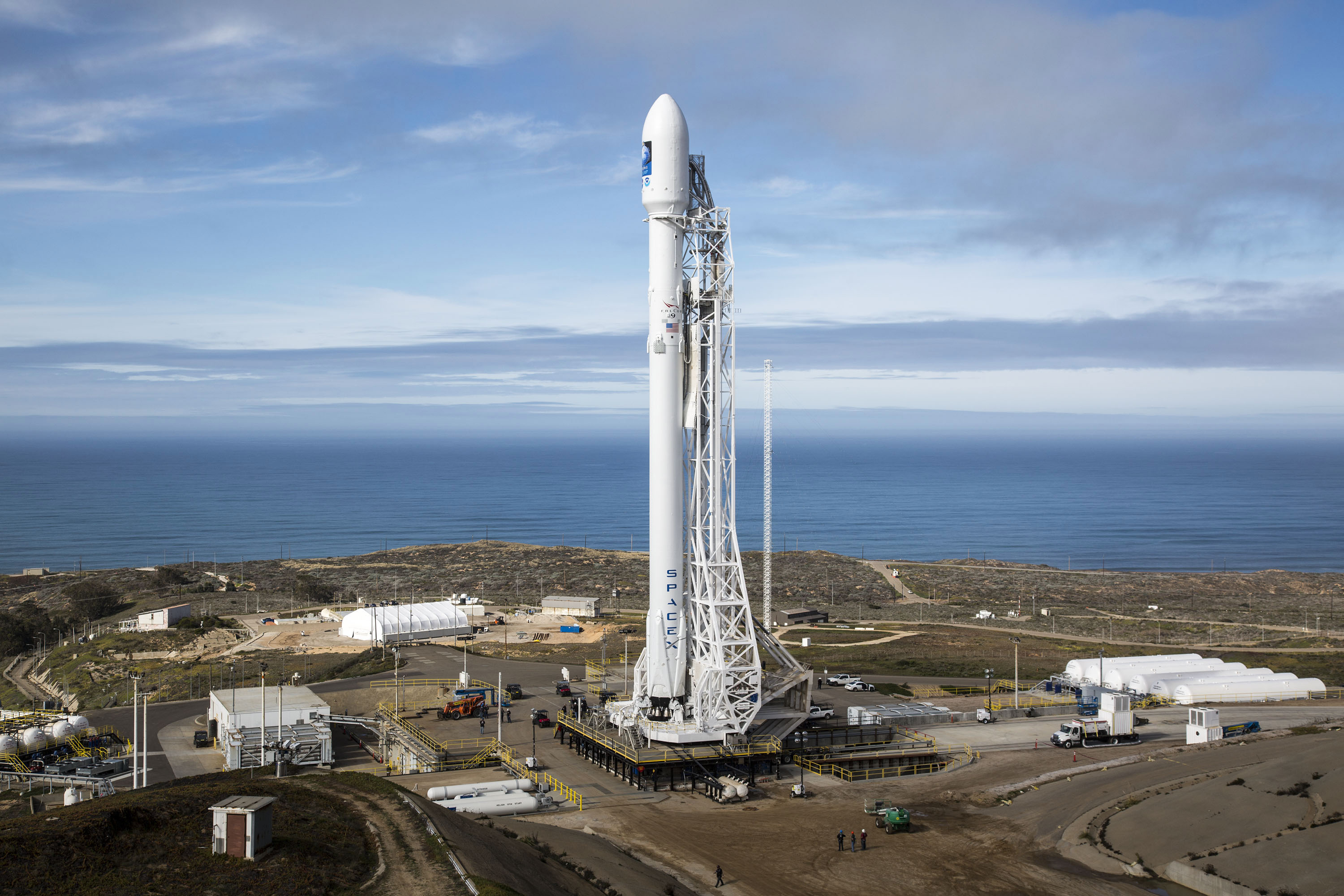 Un cohete Falcon 9 de SpaceX en posición vertical en la plataforma de lanzamiento de Vandenberg, con el mar al fondo
